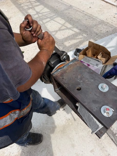 Worker tightening a bolt on a metal cart outdoors beside tools and a brown paper bag.