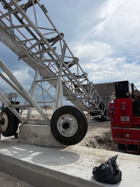 Large metal conveyor or crane structure with wheels beside a red truck on a construction site.