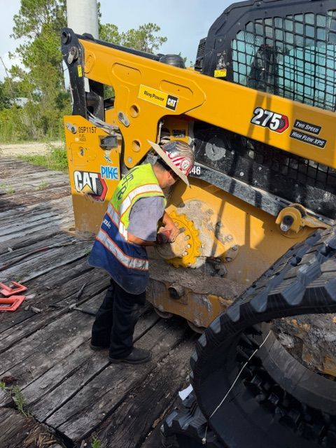 Worker in safety vest inspecting a yellow CAT machine on a wooden deck outdoors