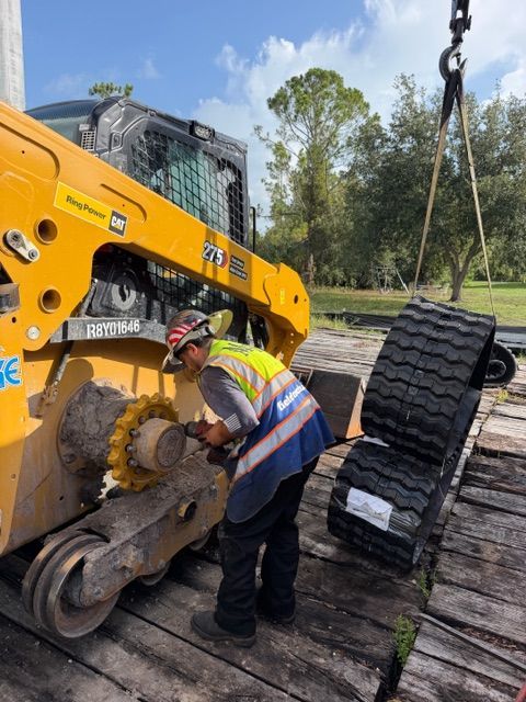 Worker in safety vest guiding a skid steer while lifting black rubber tracks outdoors