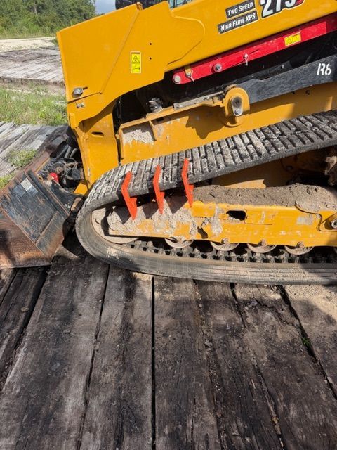 Yellow tracked construction machine on a wooden surface, close-up of its side and undercarriage.