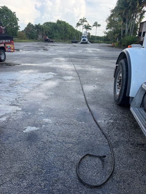 Cracked concrete parking lot with parked vehicles and trees in the background, a loose cable lying on the ground.