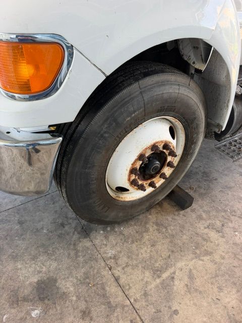 Close-up of a white truck’s front wheel with a flat tire and rusted hub on a concrete floor