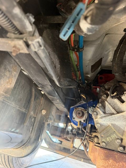 Underbody view of vehicle machinery with metal pipes, wires, and a blue component in a cramped space