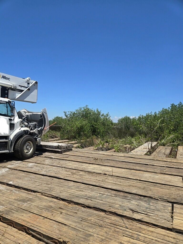 White truck unloading lumber onto a flatbed on a sunny dirt site under a clear blue sky