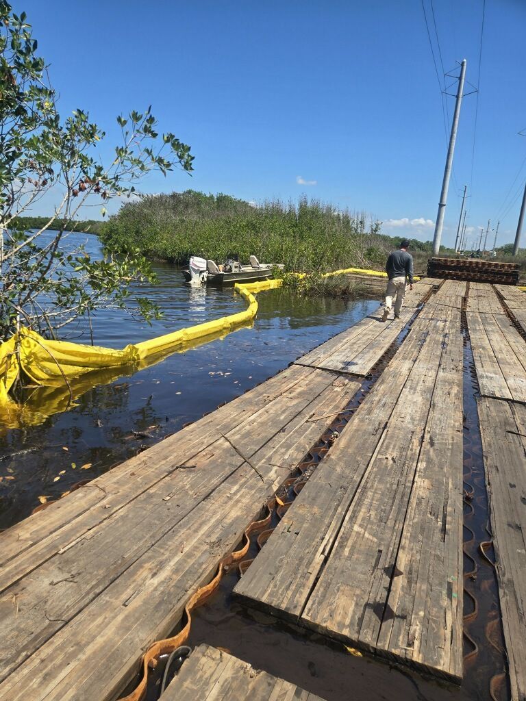 Wooden dock beside flooded water with yellow boom barrier and a person walking along the pier