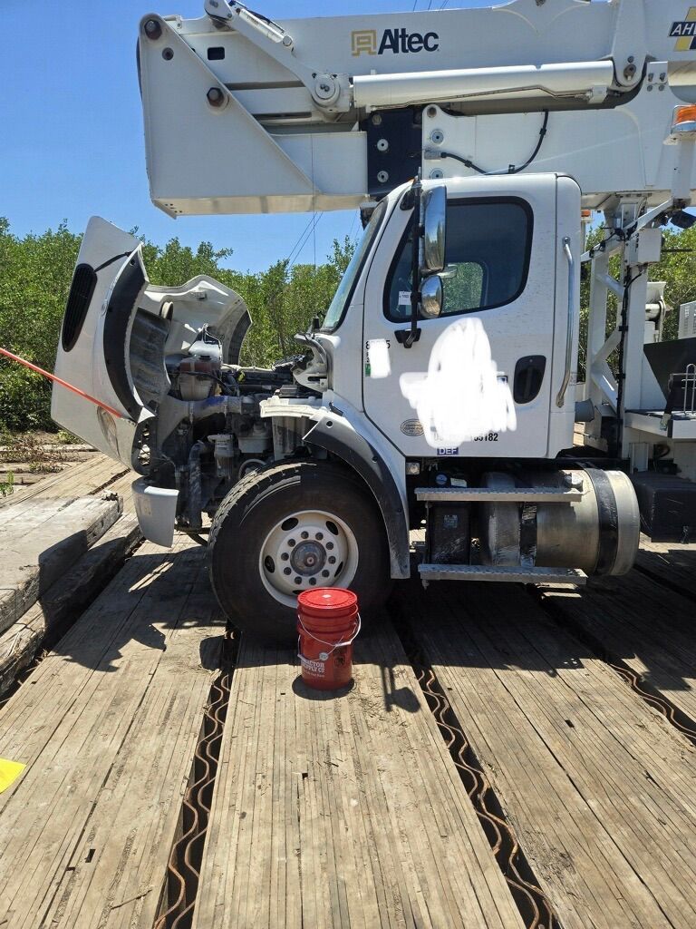 White utility bucket truck with hood open on a wooden work platform in sunny outdoor setting