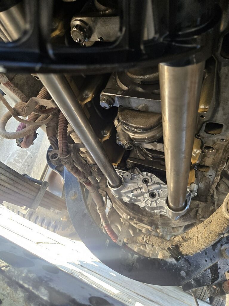 Under a vehicle, showing suspension, drive shaft, and wheel hub in a muddy undercarriage view