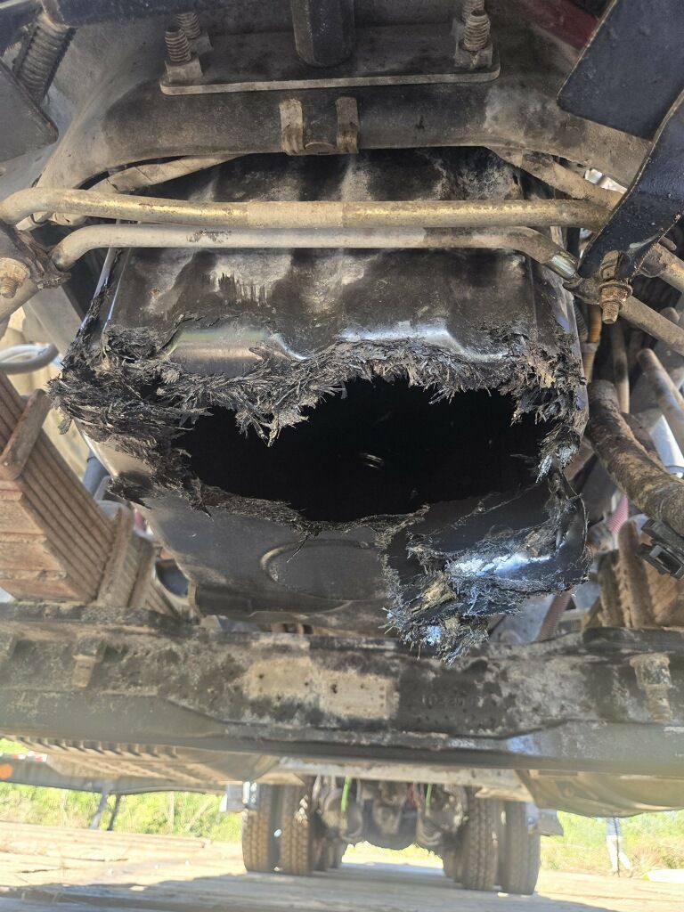 Damaged underside of a vehicle with a large burned-out hole and charred metal framing.