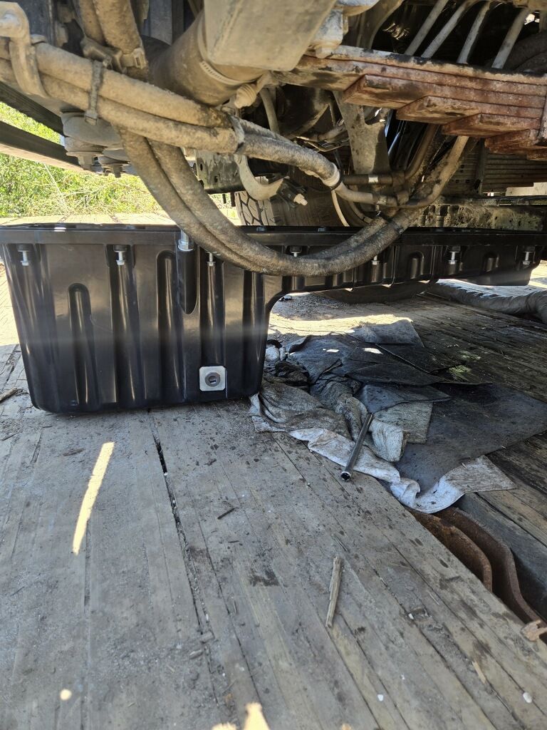 Truck undercarriage over black storage bin on a flatbed trailer, with debris and a broken hose nearby