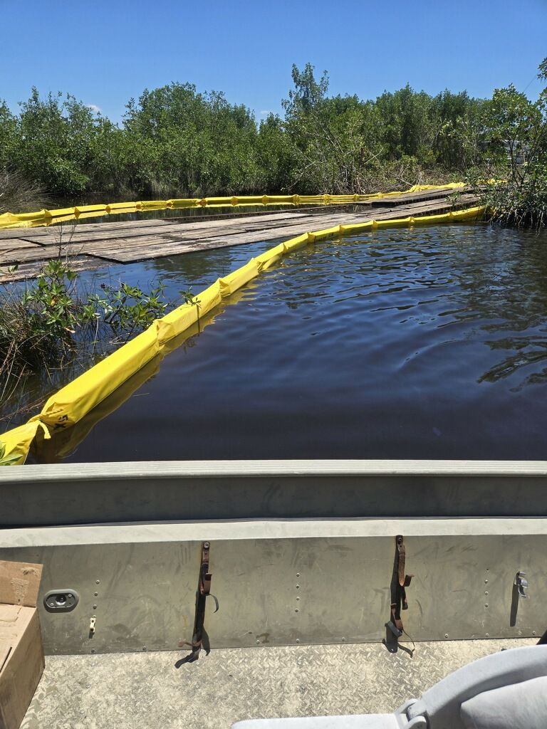 Yellow floating boom in dark water near mangroves, viewed from a small boat or dock.