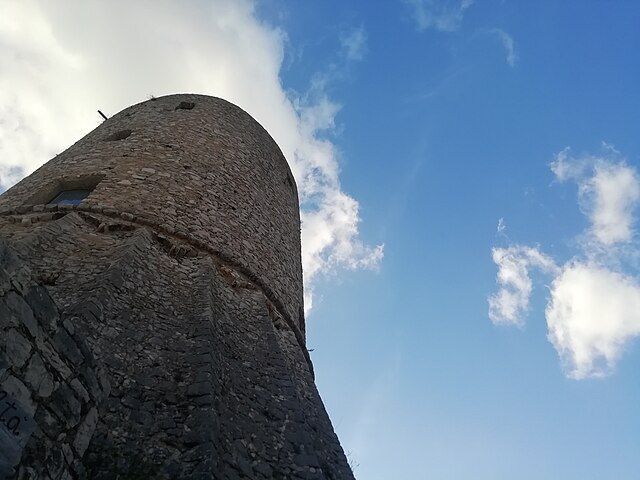 Torre di pietra contro un cielo azzurro con nuvole sparse.