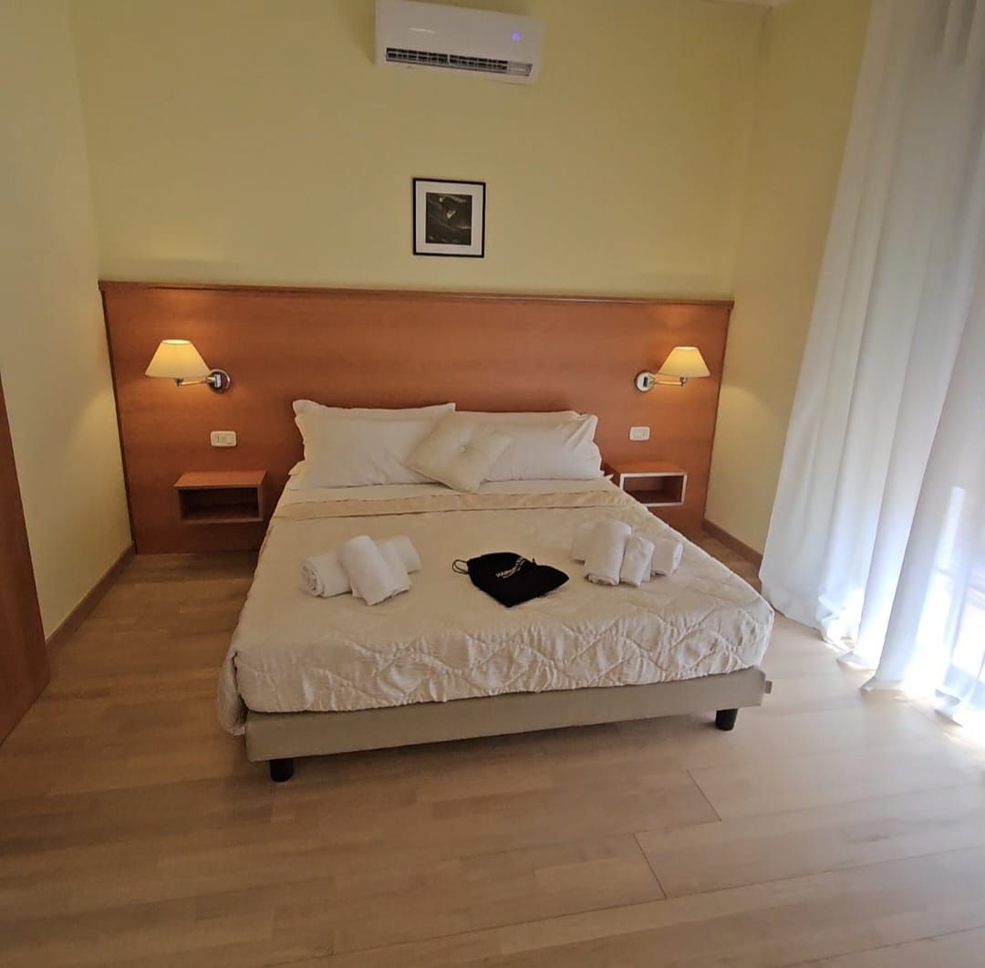 Camera d'albergo con letto, lampade e finestra con tende bianche.