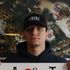 Man in black AMIRI cap and hoodie holding a sign, standing before a tiger-and-leopard mural.