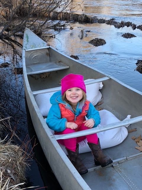 A little girl in a pink hat is sitting in a canoe.