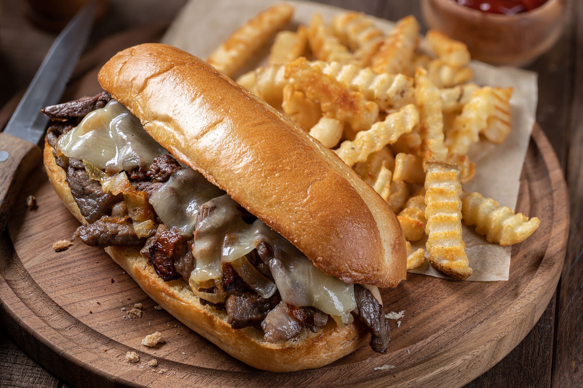 A sub sandwich with french fries on a wooden cutting board.