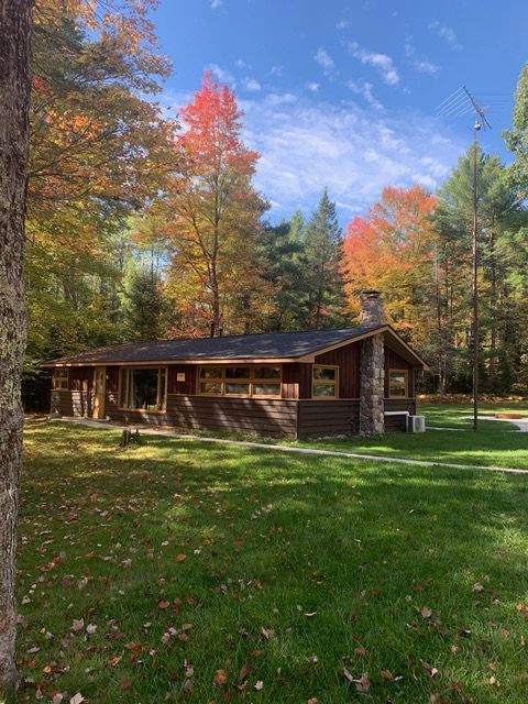 Cabin with stone chimney surrounded by colorful autumn trees on a sunny day.