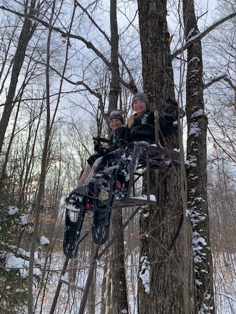 Two people are sitting in a tree with snowshoes on.