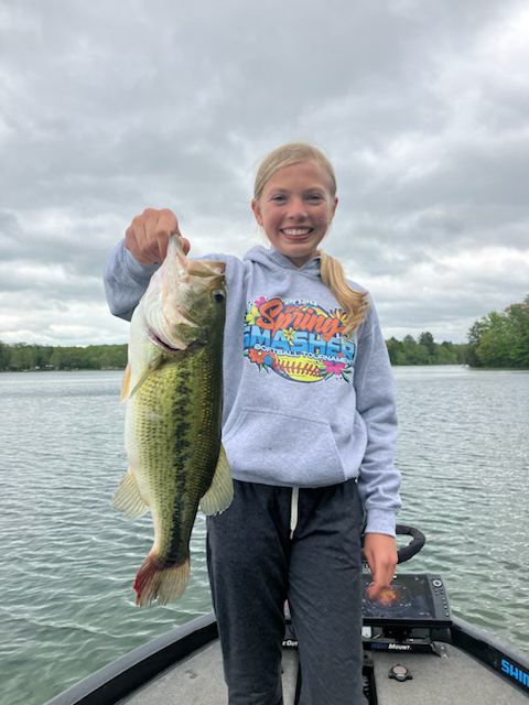 A young girl is holding a large bass on a boat.