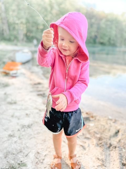 A little girl in a pink hoodie is holding a fish in her hand.