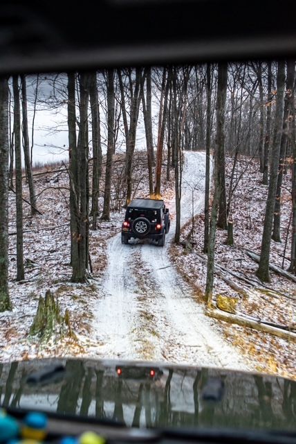 A car is driving down a snowy road in the woods.