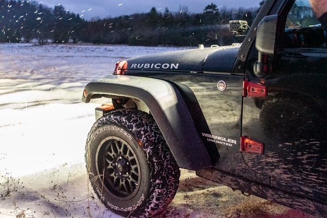 A black jeep rubicon is parked in the snow.