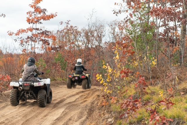 Two people are riding atvs down a dirt road in the woods.