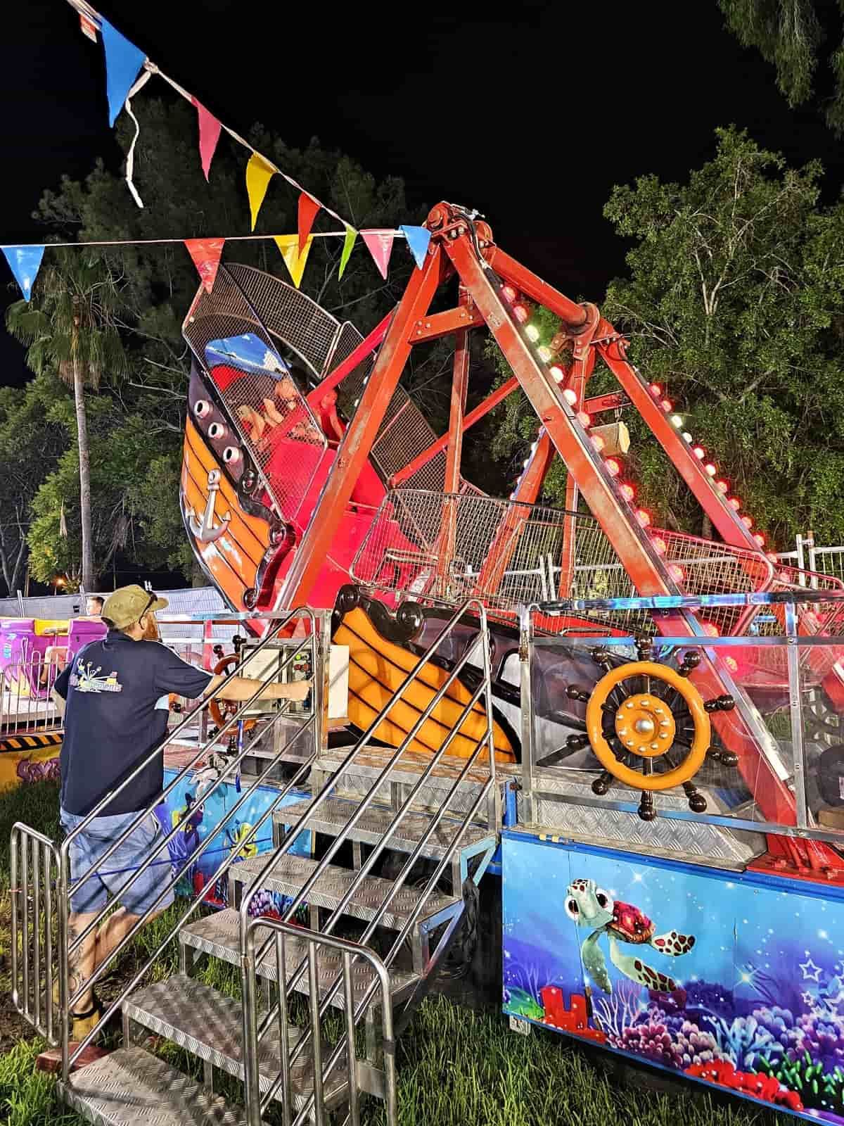 A Man Is Standing Next To A Carnival Ride At Night — Bills Amusements In Rockhampton, QLD