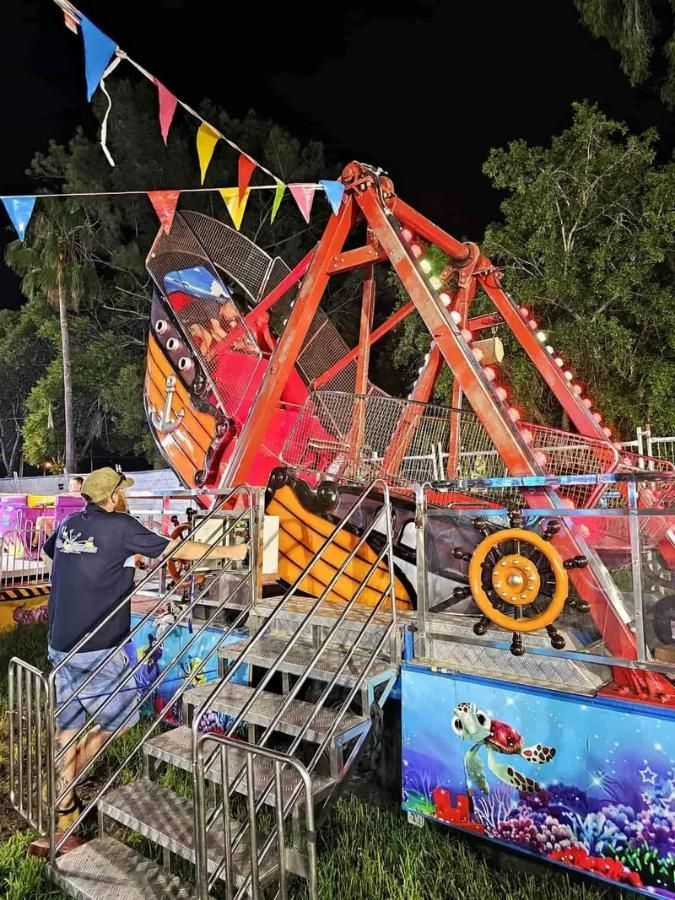 A Man Is Standing Next To A Carnival Ride At Night — Bills Amusements In Biloela, QLD
