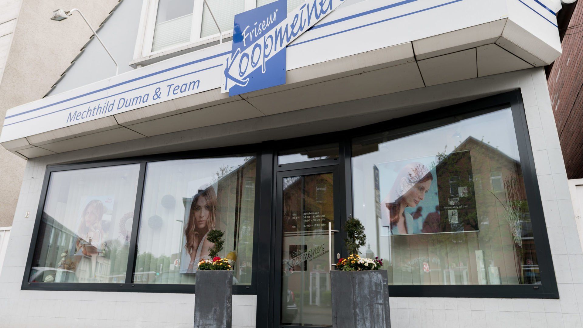 Außenansicht eines Friseursalons mit großen Fenstern, darüber ein Schild mit der Aufschrift „Frank K Koperfines“.