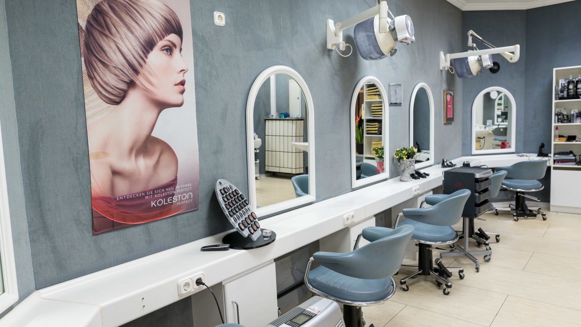 Interieur eines Friseursalons mit Styling-Stationen, Spiegeln und einem Frauenporträt.