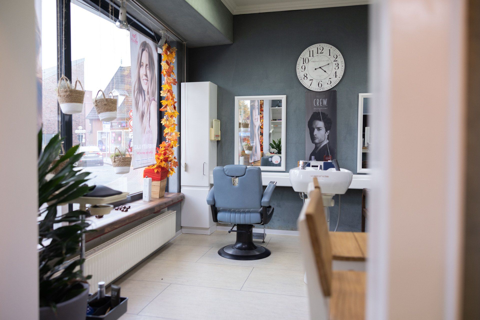 Inneneinrichtung eines Friseursalons mit blauem Stuhl, Waschbecken, Spiegel und Uhr an der Wand.