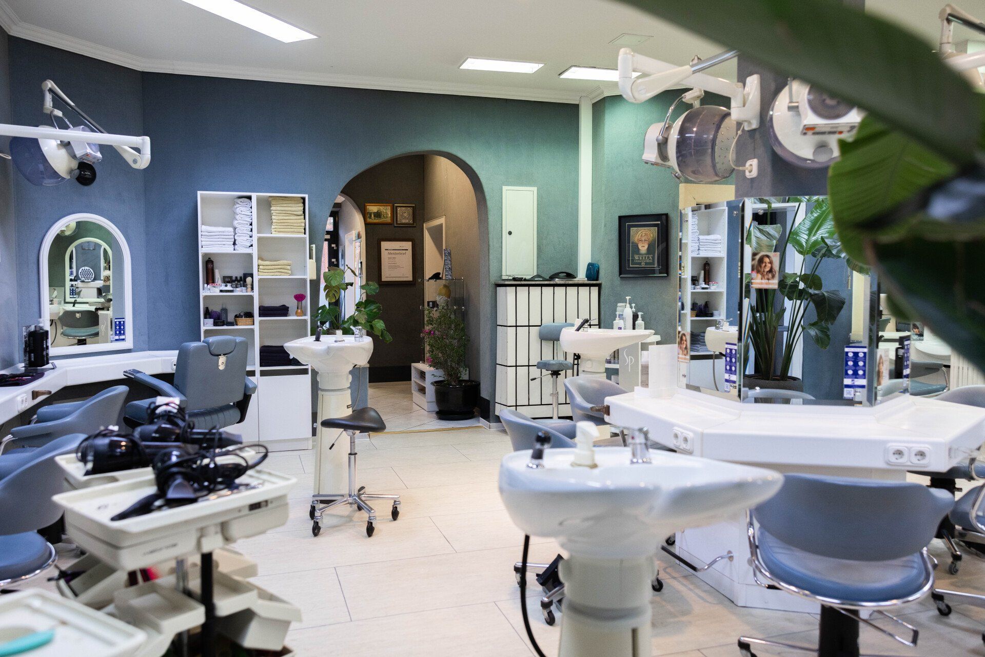 Inneneinrichtung eines Friseursalons mit Styling-Stationen, Waschbecken und Geräten; blaue Wände, neutrale Töne.