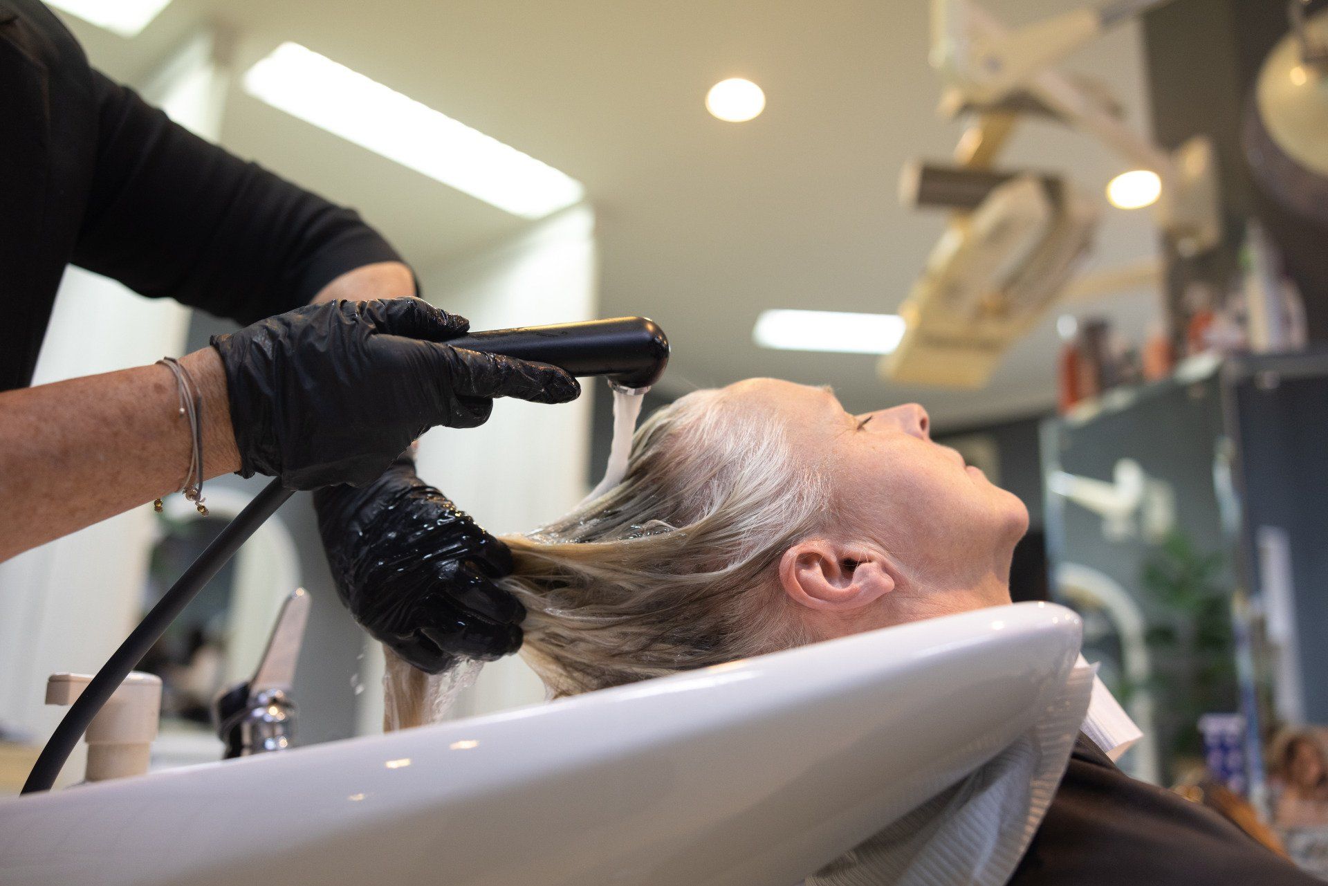 Friseur wäscht einer Frau in einem Salon die Haare. Der Friseur trägt schwarze Handschuhe.
