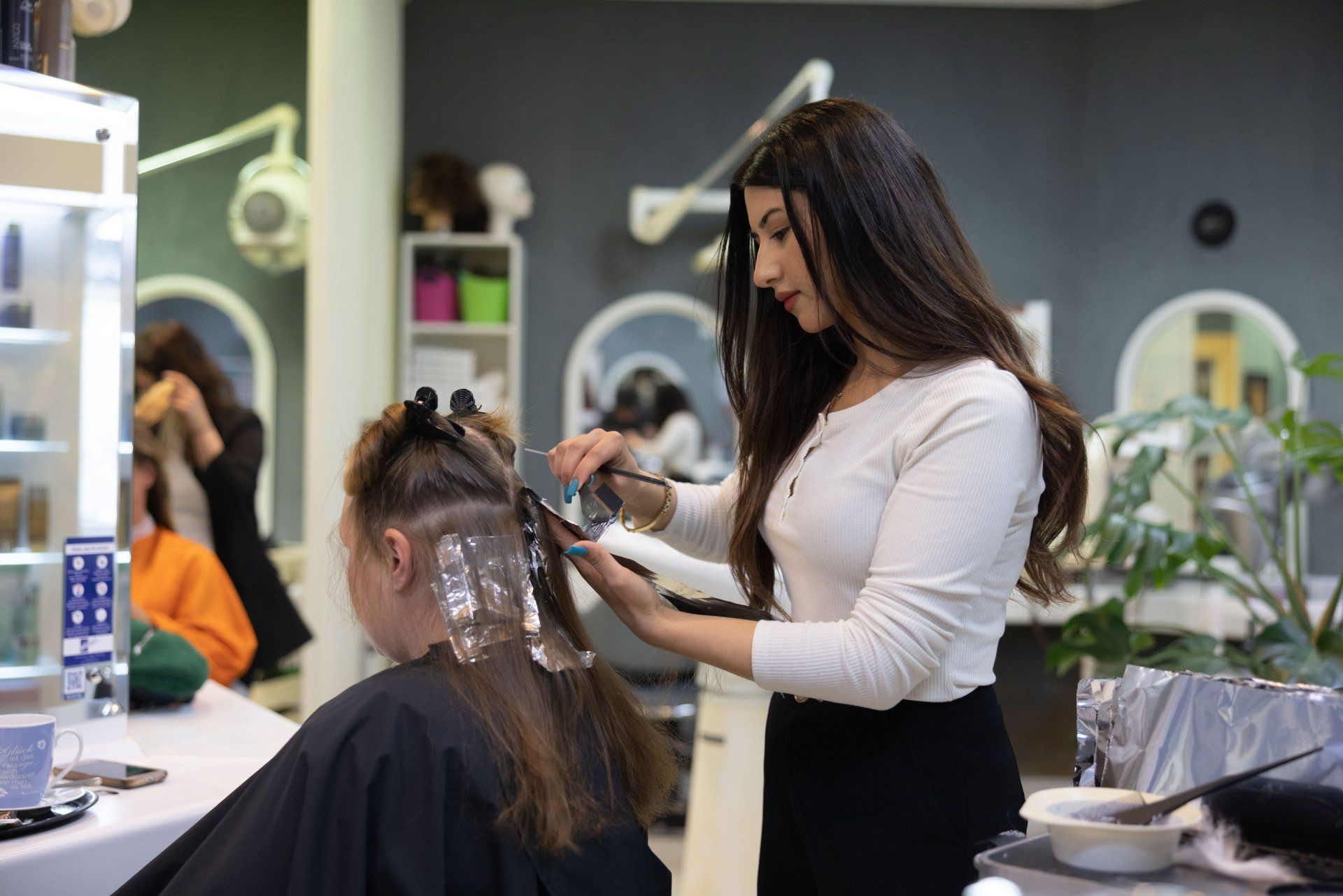 Friseur bringt in einem Salon Strähnchen in das Haar einer Kundin.