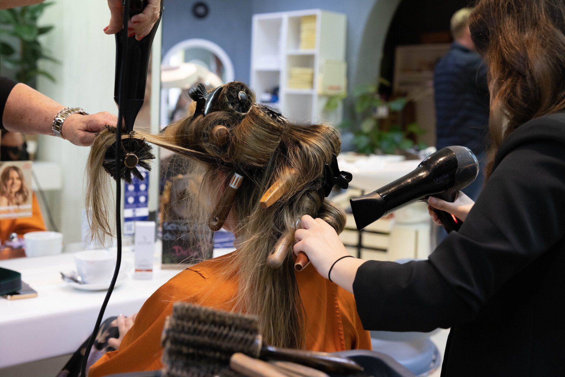 Zwei Stylisten föhnen in einem Salon die Haare einer Kundin.