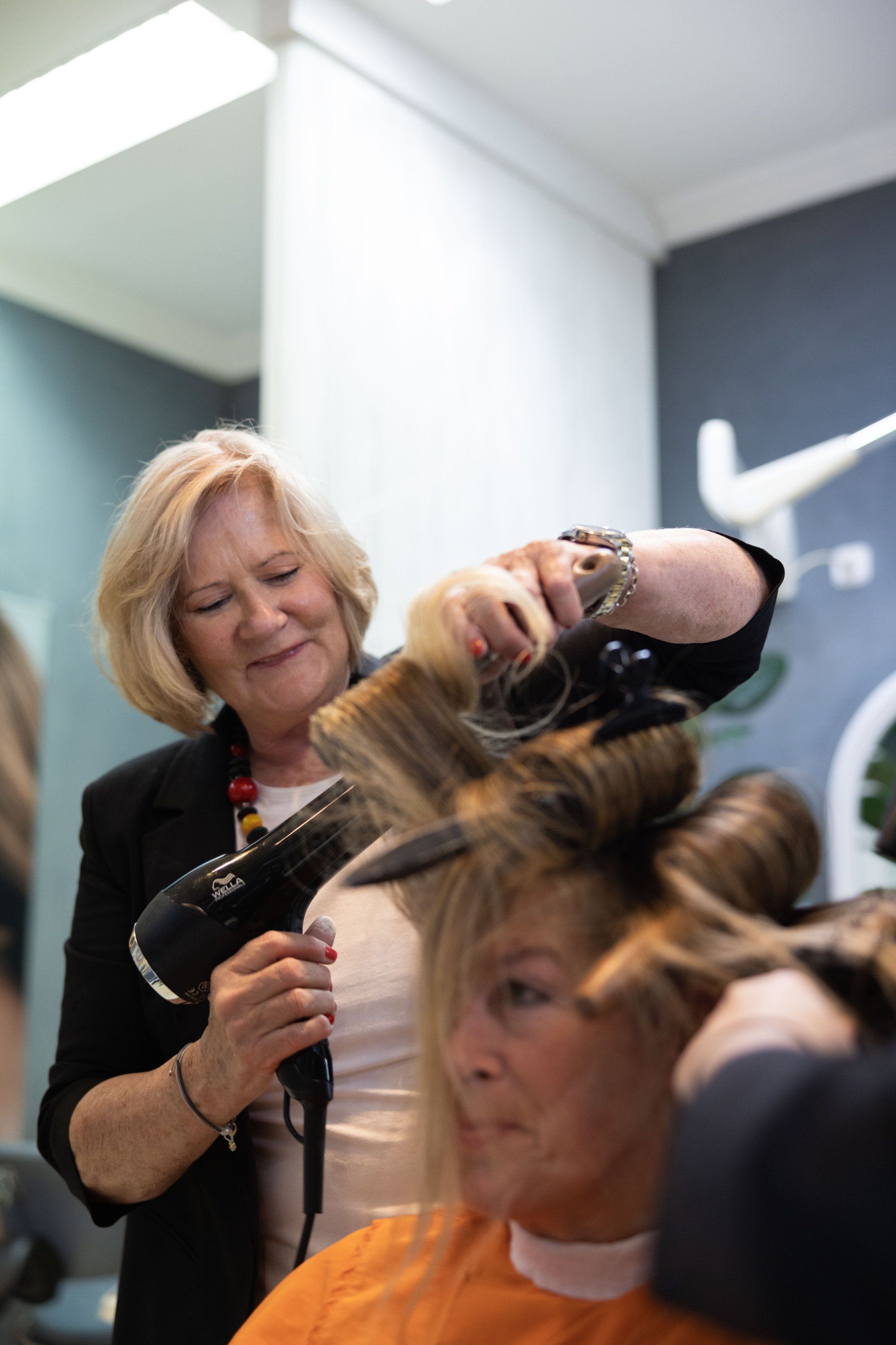 Friseur frisiert einer Frau in einem Salon mit einem Föhn die Haare.