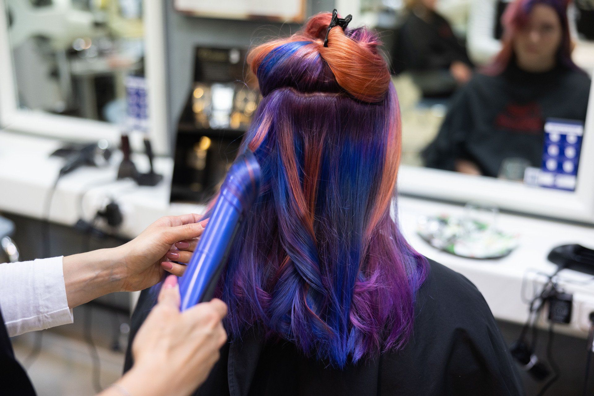 Eine Person mit buntem Haar lässt sich in einem Salon die Haare mit einem Glätteisen stylen.