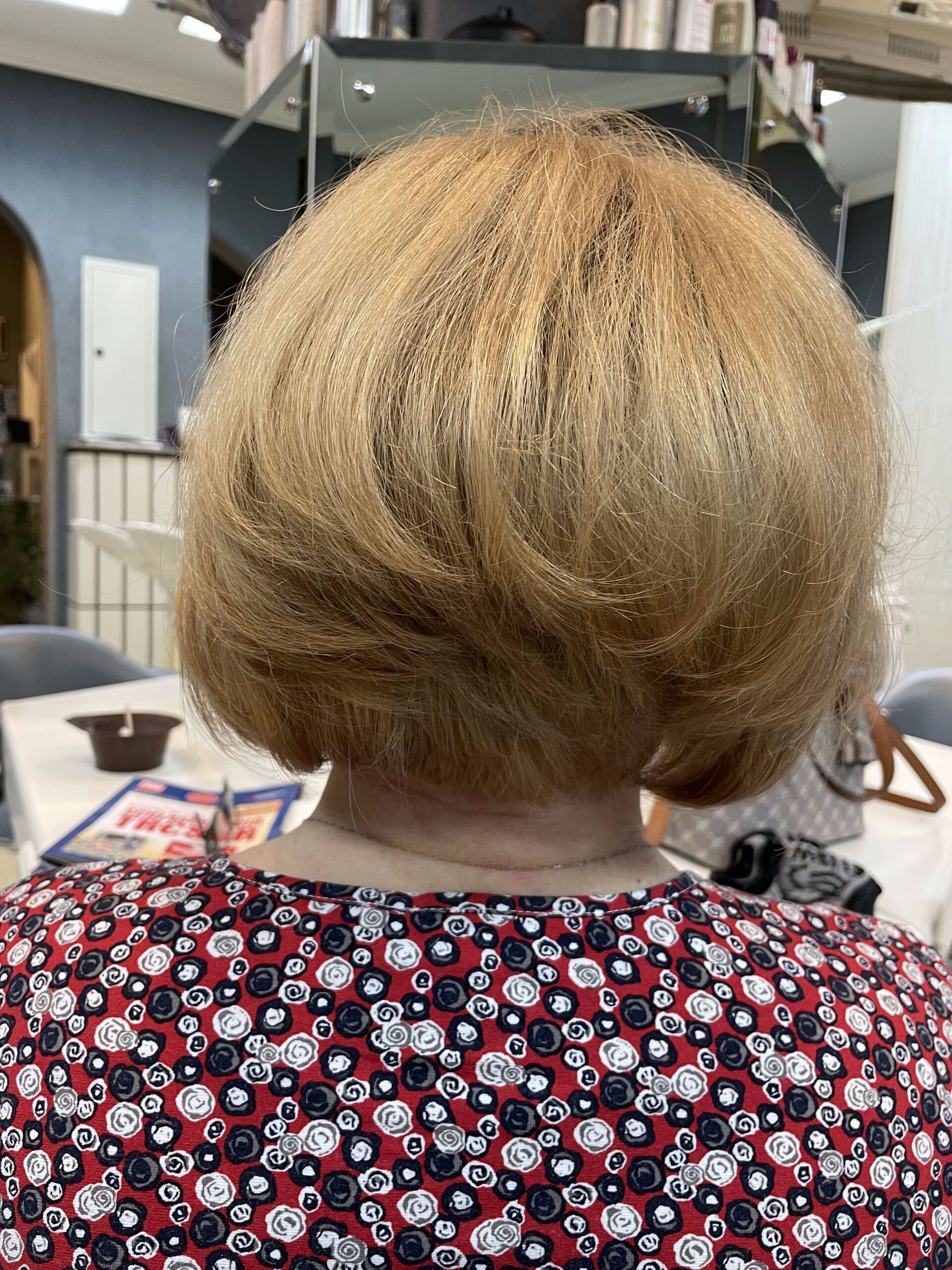 Frau mit hellbrauner, gestufter Bob-Frisur in einem Salon, trägt ein rotes Blumentop.
