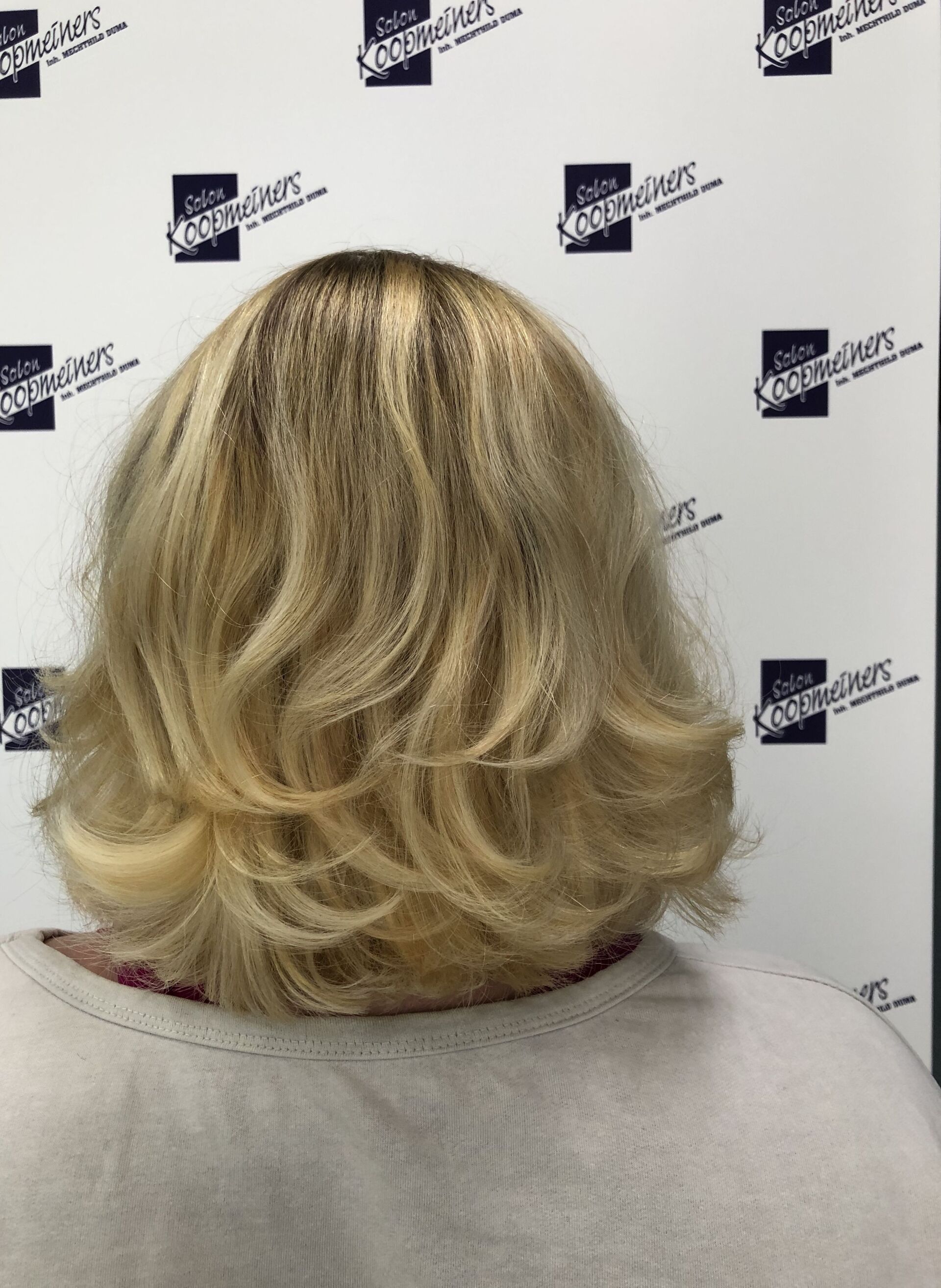Blonder gestufter Bob mit dunklem Ansatz, von hinten betrachtet.