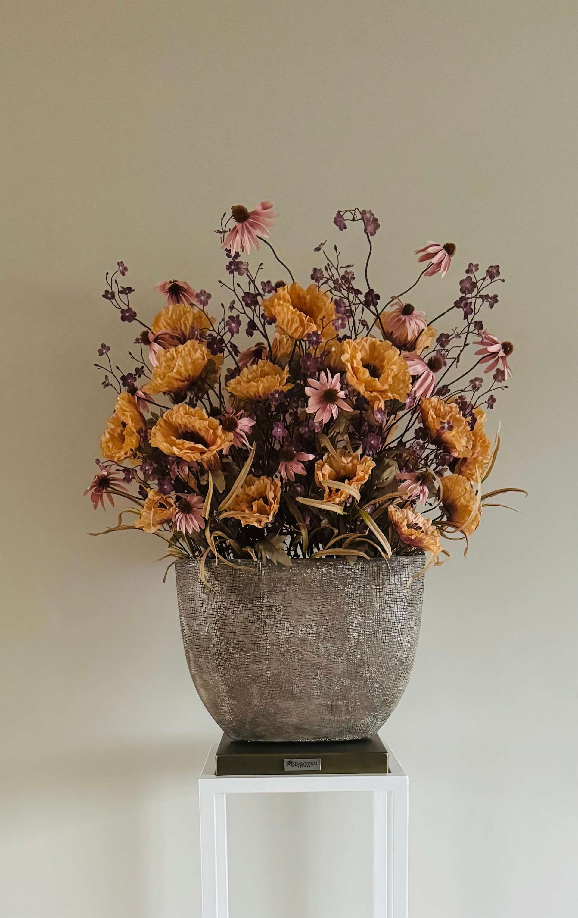 Op een houten tafel staat een witte vaas gevuld met bloemen.