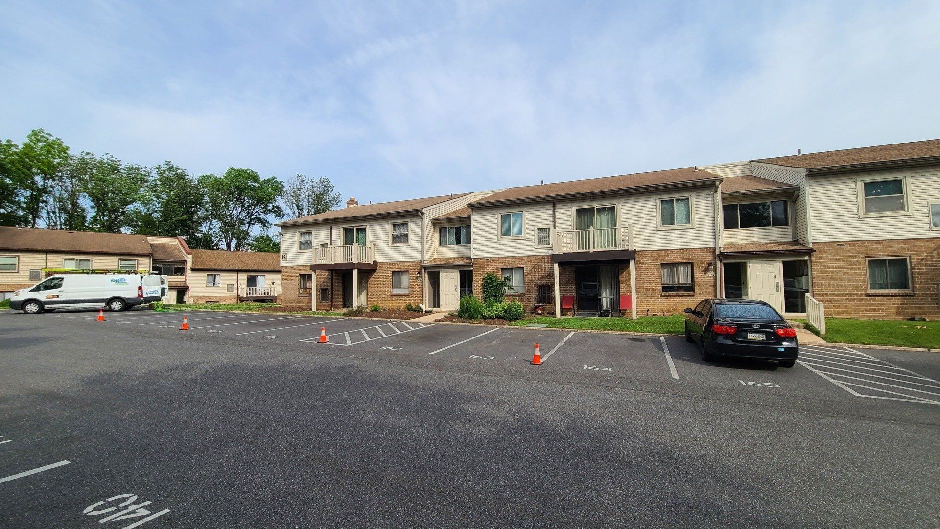 Apartment building with parking lot; cars parked, orange cones, overcast sky.