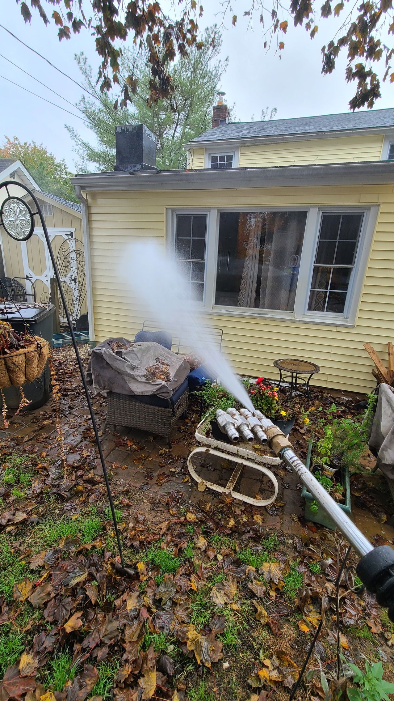 Pressure washer spraying a yellow house exterior with fallen leaves on the ground