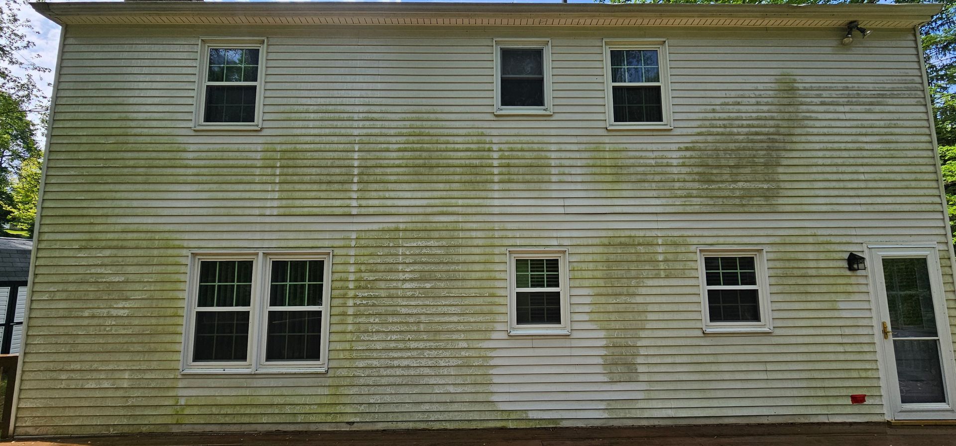 White two-story house with faded siding, several windows, and visible weather staining near the roofline.