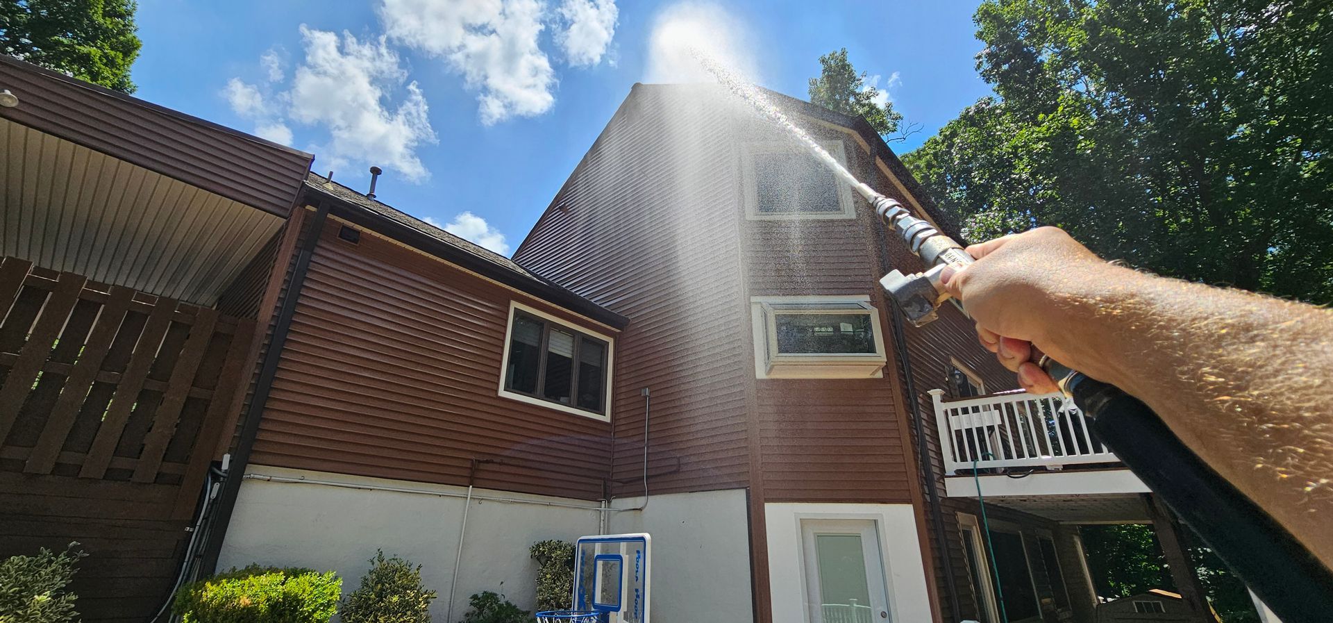 Spraying water up at a brick house with a roof under bright sun and blue sky