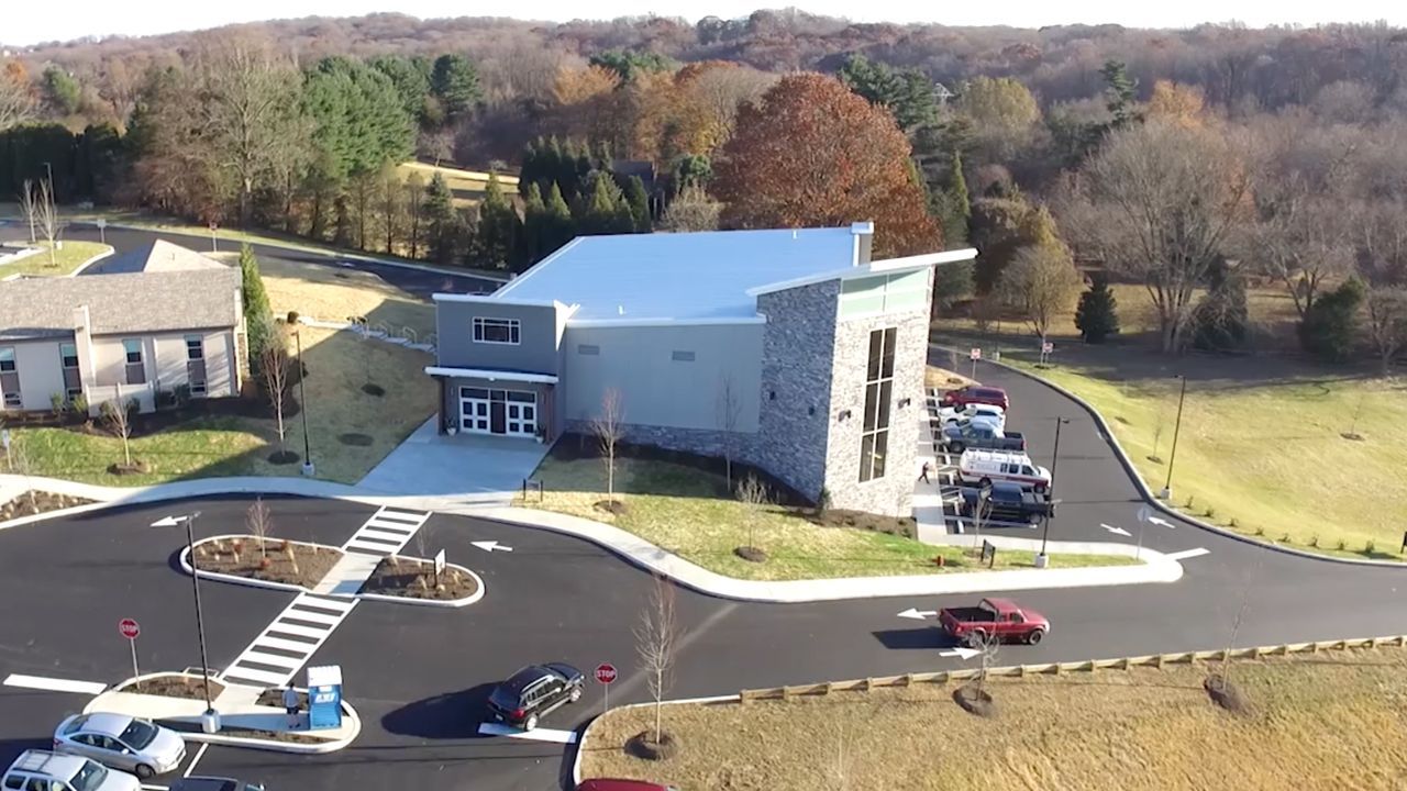 Modern building with angular roof, stone facade, and parking area. Cars are parked.