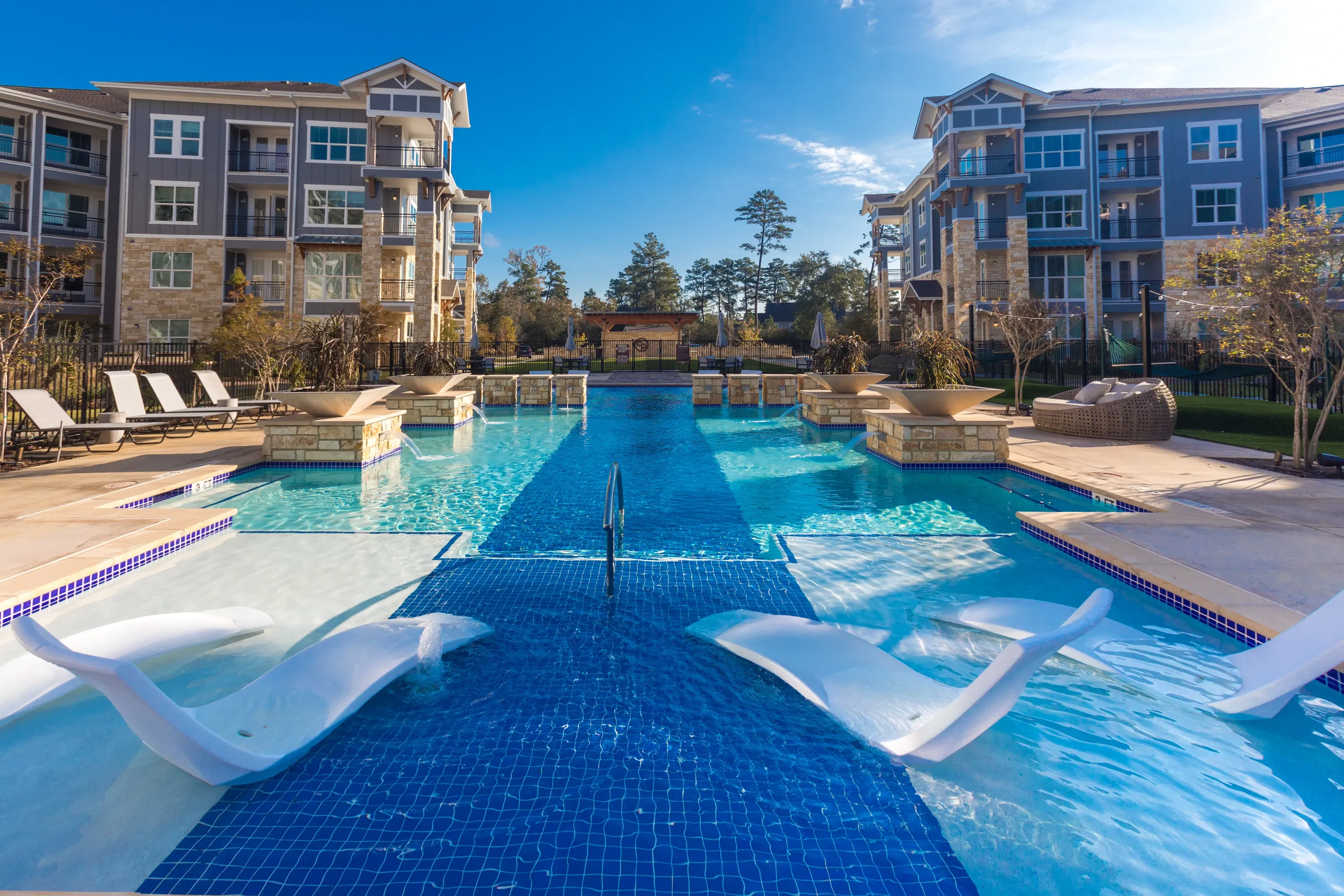 Modern apartment complex pool with lounge chairs and modern chaise lounges.