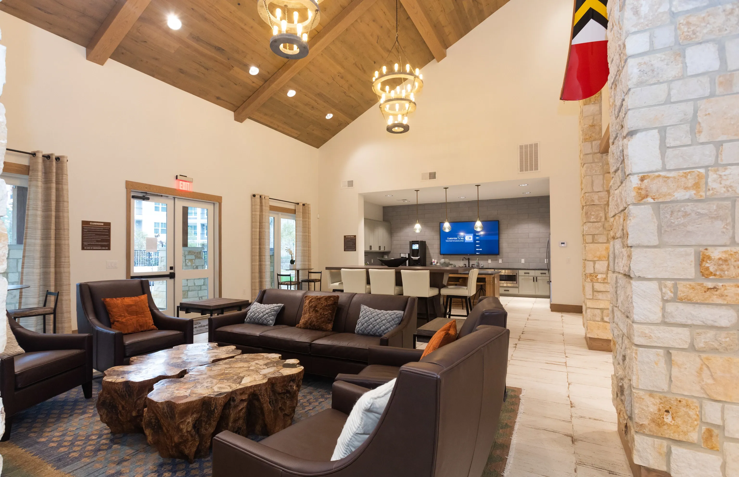 Spacious community lounge area with leather sofas, unique tree trunk coffee tables, and a modern kitchen/bar in the background.