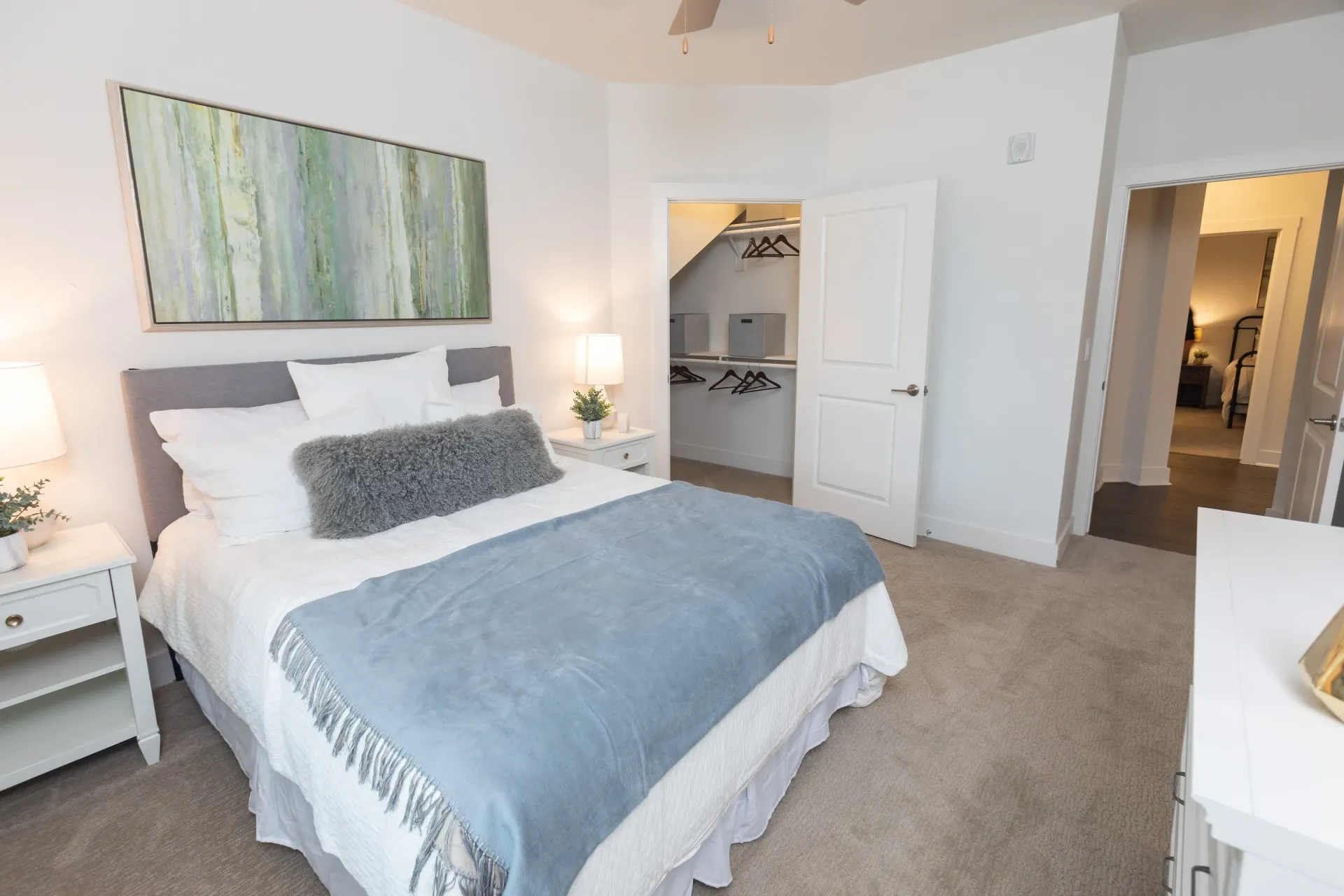 Bedroom with a queen-size bed, nightstand, walk-in closet, and an open doorway to another room.