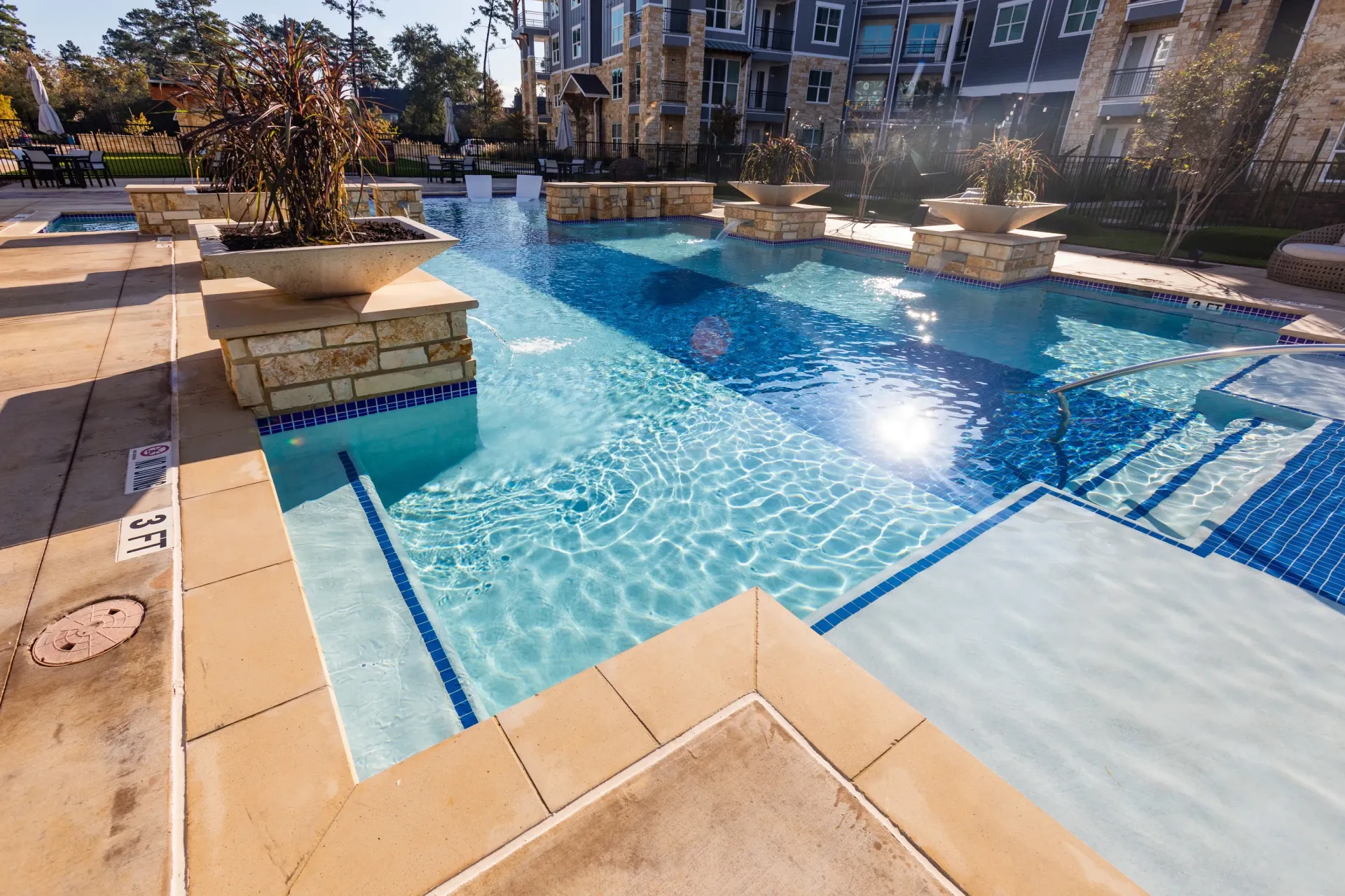 Luxury swimming pool and spa area with lounge seating and modern apartment buildings in the background.